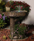 Solar Powered Bird Fountain With Birdhouse And LED Lights For Easy Setup Outdoor Gardens 29.5 Inch Resin Waterfall Feature Gentle Single Tier Water Flow For Patio And Yard Rustic Bird Bath. Visible: rustic resin structure with solar fountain and birdhouse feature, surrounded by plants.