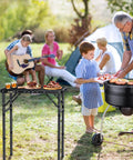 Folding Grill Table For Camping And BBQ, Aluminum Outdoor Table with adjustable height, holding food next to family campfire scene, 22.8x16 in, Black.