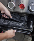 Person cleaning ash tray of Genesis E 325 Liquid Propane Gas Grill For Outdoor Cooking With Three Burners Black Porcelain Enameled Cast Iron Grates PureBlu Burners And Sear Zone To Level Up Your Grill Game And Extra Grilling Space.