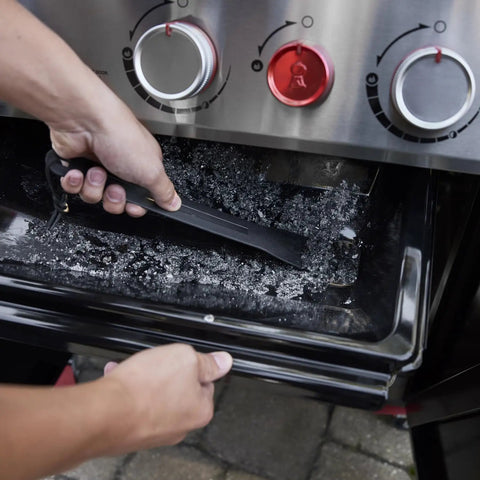 Person cleaning ash tray of Genesis E 325 Liquid Propane Gas Grill For Outdoor Cooking With Three Burners Black Porcelain Enameled Cast Iron Grates PureBlu Burners And Sear Zone To Level Up Your Grill Game And Extra Grilling Space.