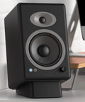 Black angled desktop speaker stands with anti slip silicone wedges for medium speakers, setup with monitor on desk.