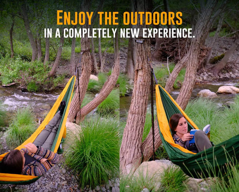 Two people in Cozy Two Person Camping Hammock With Bug Net And Rain Fly, lounging by a stream in a forested area.