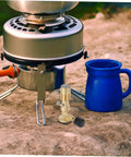 Portable Gas Blowtorch Head For Camping And Outdoor Cooking with Brass Construction next to stove and blue mug