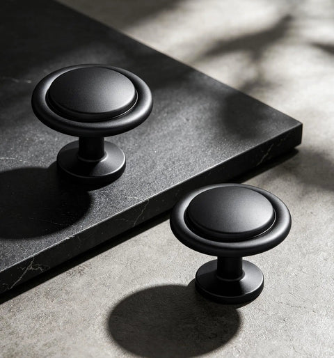 Matte Black Round Euro Style Cabinet Knobs One And One Quarter Inch 30 Pack Upgrade Your Cabinets Dresser Drawers Vanities And Coordinating With Appliances Faucets And Hardware Durable Finish And Easy Installation For Makeover Updates In Kitchen Or Bath. Two matte black round cabinet knobs on a stone surface