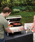 Two men using the Chef's Style Tabletop Portable Propane Grill With 20,000 BTU Stainless Steel Two-Burner Outdoor Gas Grill.