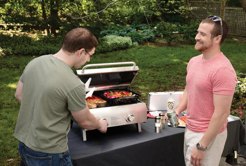 Two men using the Chef's Style Tabletop Portable Propane Grill With 20,000 BTU Stainless Steel Two-Burner Outdoor Gas Grill.