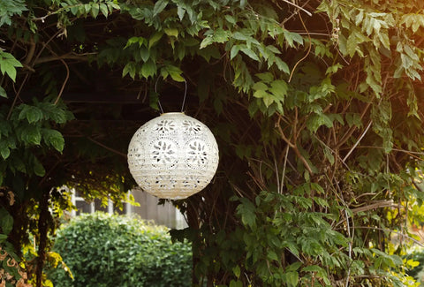 LED Outdoor Solar Lantern For Patio And Deck Handmade Tyvek Weather Resistant UV Rated Stainless Steel Hardware Auto Sensor On Off Energy Efficient Garden Light That Is Lit In Pearl hanging among green foliage.