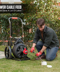Person using 100 Foot Auto Feed Electric Drain Snake Auger For 2 To 4 Inch Pipes to clear a drain outdoors.