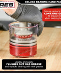 Deluxe Bearing Packer in use, removing old grease from a bearing, showcasing universal fit for bearings up to 3.5 inches in a clear polycarbonate body.