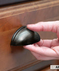 Hand installing oil rubbed bronze cabinet cup pull on wooden drawer, part of the Oil Rubbed Bronze Cabinet Cup Pulls Three And A Half Inch Overall Length 10 Pack Durable Drawer Handles With Optional One Inch And One And Three Quarter Inch Mounting Lengths Ideal For Kitchen And Bath Cabinets And Furniture Projects.