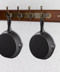 Two mini cast iron skillets hanging on a wall hook, part of the Four Pack Mini Cast Iron Skillets 4 Inch With Double Drip Spouts