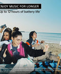 Group of friends at the beach enjoying music with the Ultimate Field 1 Waterproof Portable Bluetooth Speaker. Woman holding speaker.