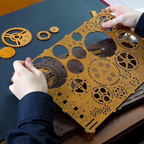 Person holding laser-cut pieces from Gear Globe Wall Clock Kit With 369 Laser Cut Pieces, DIY Wooden 3D Puzzle Clock That Builds Without Glue.