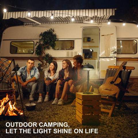 Outdoor camping scene with a Cordless Table Lamp With 5200mAh Battery, on a table beside a camper, illuminating a group of people.