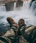 Person wearing brown shoes sitting by a waterfall with cascading water in the background