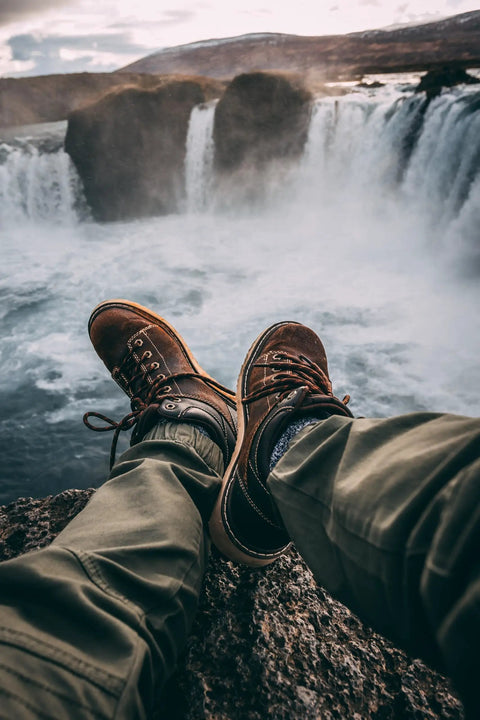 Person wearing brown shoes sitting by a waterfall with cascading water in the background