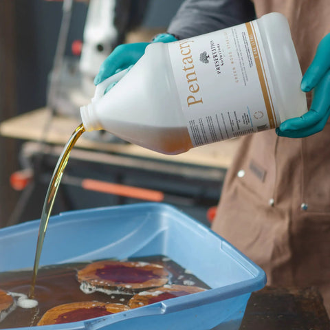 Person pouring green wood stabilizer for fresh wood into a blue container in a workshop, preventing cracking and shrinking.