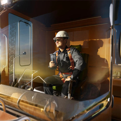 Engineer holding 20 oz tumbler, seated in construction equipment cab, wearing hardhat and harness. Engineer Gifts Tumbler 20Oz For Mechanical Engineers And Civil Engineers Gift For Men Graduation Day Keepsake That Combines Practical Coffee Insulation With Geeky Style.