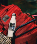Snag Our Fly Custom 17 Oz Insulated Water Bottles With Double Wall Stainless Steel Build Plus Leak Proof Reusable Design Great For Sports Travel And Gym Workouts White Bulk 100 Pack Holds One Hundred Cups Ideal Kick Back Drinkware Vacuum Sealed next to a red backpack.