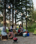 97 Ft White Outdoor String Lights With 49 Shatterproof G40 LED Bulbs hanging above a campfire gathering in a forest setting.