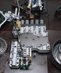 Automotive transmission components on workshop floor with assorted gears and parts, focus on metal assembly, no rings visible