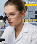 12 Pack Clear Safety Glasses Bulk With Kickass Scratch Resistant Polycarbonate Lenses And Sweet Uv Protection For Heavy Duty Job Sites And Weekend Diy Projects Rock Solid Ansi Z87 Approved worn by a woman using a microscope in a lab.