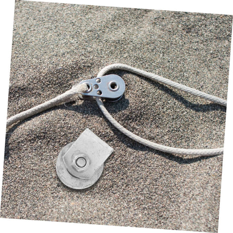 Two cast-iron garage door hardware pieces: groove wheel roller and rope pulley on sandy surface