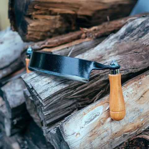 Heavy Duty Eight Inch Curved Draw Shave Tool resting on logs, showcasing durable carbon steel edge and wooden handle.