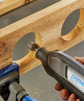 Close-up of Dremel 8240 cordless rotary tool in hand, gray/black body with blue branding, grinding wood.