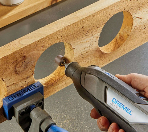Close-up of Dremel 8240 cordless rotary tool in hand, gray/black body with blue branding, grinding wood.