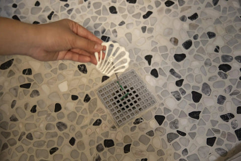 Person using Disposable Hair Stopper For Shower, Sink, And Tub - Hygienic No-Touch Hair Cleanup, fits drain, Ocean White design.