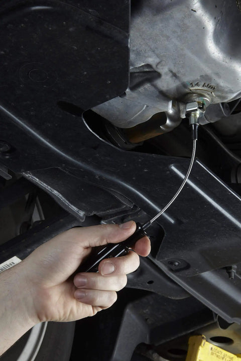 Using the Drain Plug Pro Tool Kit With Interchangeable Attachments For Standard Low Profile And Internal Hex Plugs under a car.