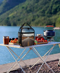 Reusable Insulated Lunch Box With Side Pocket And Detachable Handle for picnics by a lake with fruit and camping gear on table