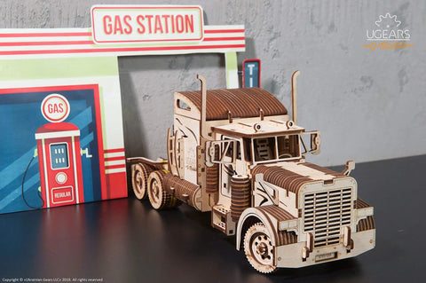 Mechanical 3D Wooden Puzzle Heavy Boy Truck VM-03 Model Kit For Adults And Teens, Realistic Gear Driven 18-Wheeler Build With Key Start, A Beast Of A Wooden Rig For Builders, Collectors, And Truck Fans. Wooden truck model beside gas station backdrop.