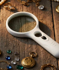 Handheld Magnifier With Light 3X And 45X Dual Magnification Loupe 3 LED Illumination For Reading Small Print Jewelry Inspection And Hobby Crafts White, placed on wooden surface with jewelry items.