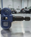 Wireless Bluetooth TPMS Tire Pressure Monitor with metal valve stem for Tesla vehicles, side view on silver surface.