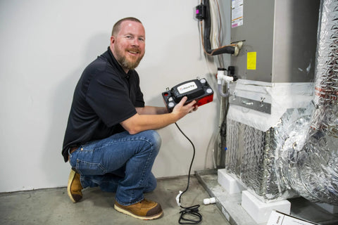 Front view of a technician kneeling beside a black-and-red Diversitech ULTRACP-22 automatic condensate pump for HVAC/R.