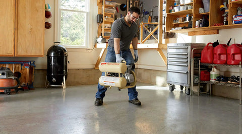 Man lifting a 2 HP Portable Twin Stack Air Compressor Powers Through Tough Jobs With Amped Up 3.2 CFM Performance in garage.