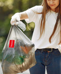 Woman holds trash bag with Trash Stickers 300 Pack 3x2 Inch Red Labels With Bold White TRASH For Bins In Home Office And Warehouse Glossy Paper Roll Easy Disposal Reminder Signage