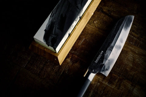 Toishi Sharpening Whetstone With 1000 And 3000 Grit For Knife Edge Maintenance on bamboo stand with chef's knife beside it
