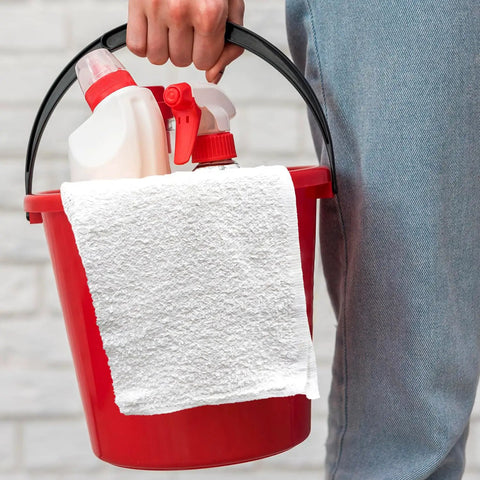Person holding a red bucket with cleaning spray bottles and a white Bar Mop Towels Value Pack Of 60, 14 By 17 Inches, Absorbent And Durable Multipurpose Cleaning Rags, Cotton Terry Cloth Towels, Reusable Shop Rags, White, Eco Friendly And Made From Recycled Cotton For Everyday Cleanup draped over the edge.