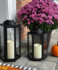 Outdoor Solar Powered Lantern With Flameless Candle For Porch Or Patio, black metal and glass design, near flowers and pumpkin