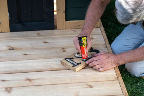 Loctite PL Premium polyurethane construction adhesive tube (4 oz) being squeezed onto wooden letters on a deck