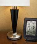 Wireless Weather Station With Wind Sensor For Backyard Forecasts And Atomic Clock Time Sync next to a table lamp