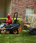 Push And Tow Lawn Roller With Ergonomic Handle And Scraper Bar attached to a lawn tractor in a yard with grass and shrubs