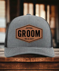 Gray trucker hat on table with 'Nathan Groom 08.24.2024' text, part of Groom Gifts For Men Customizable Groom Squad Hat Sets From 3 To 10.