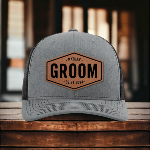 Gray trucker hat on table with 'Nathan Groom 08.24.2024' text, part of Groom Gifts For Men Customizable Groom Squad Hat Sets From 3 To 10.
