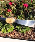 All Purpose Garden Pick Mattock Hoe With Wooden Handle 15.7 Inch Forged Adze Pick resting on garden soil among flowers