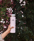 Person holding AeroLight Transit Bottle 20 Oz With Locking Lid And Leak Resistant Design in Rose Quartz Glimmer near flowers