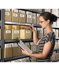 Person organizing labeled files on shelves; Ultra Fast Network Label Printer With Bluetooth And Ethernet Wireless Connectivity Slick Monochrome Printing Up To One Hundred Ten Labels Per Minute Dead Simple Setup For Professional Workflows.